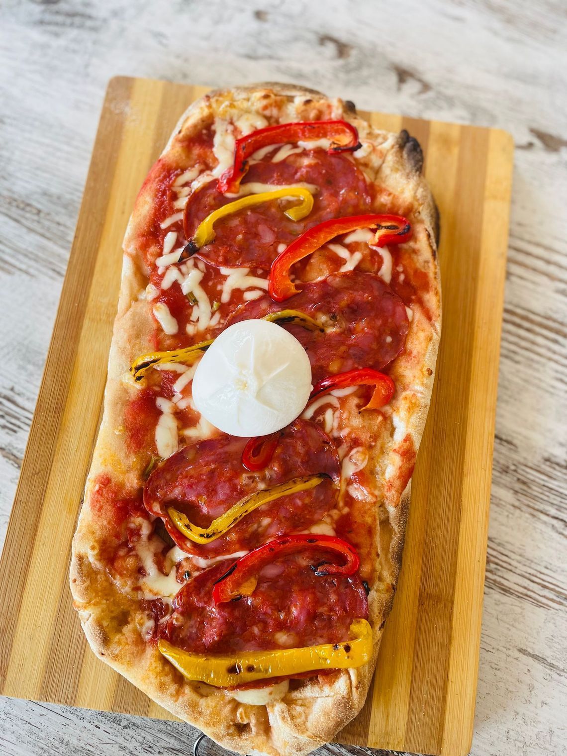 una pizza con peperoni e mozzarella su un tagliere di legno