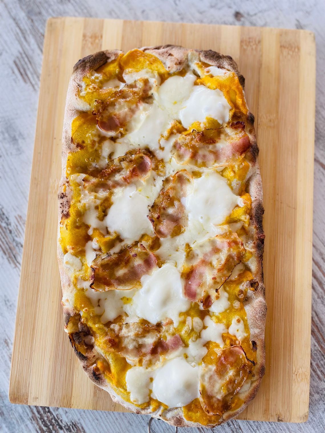 una pizza con funghi e prosciutto è su un tagliere di legno