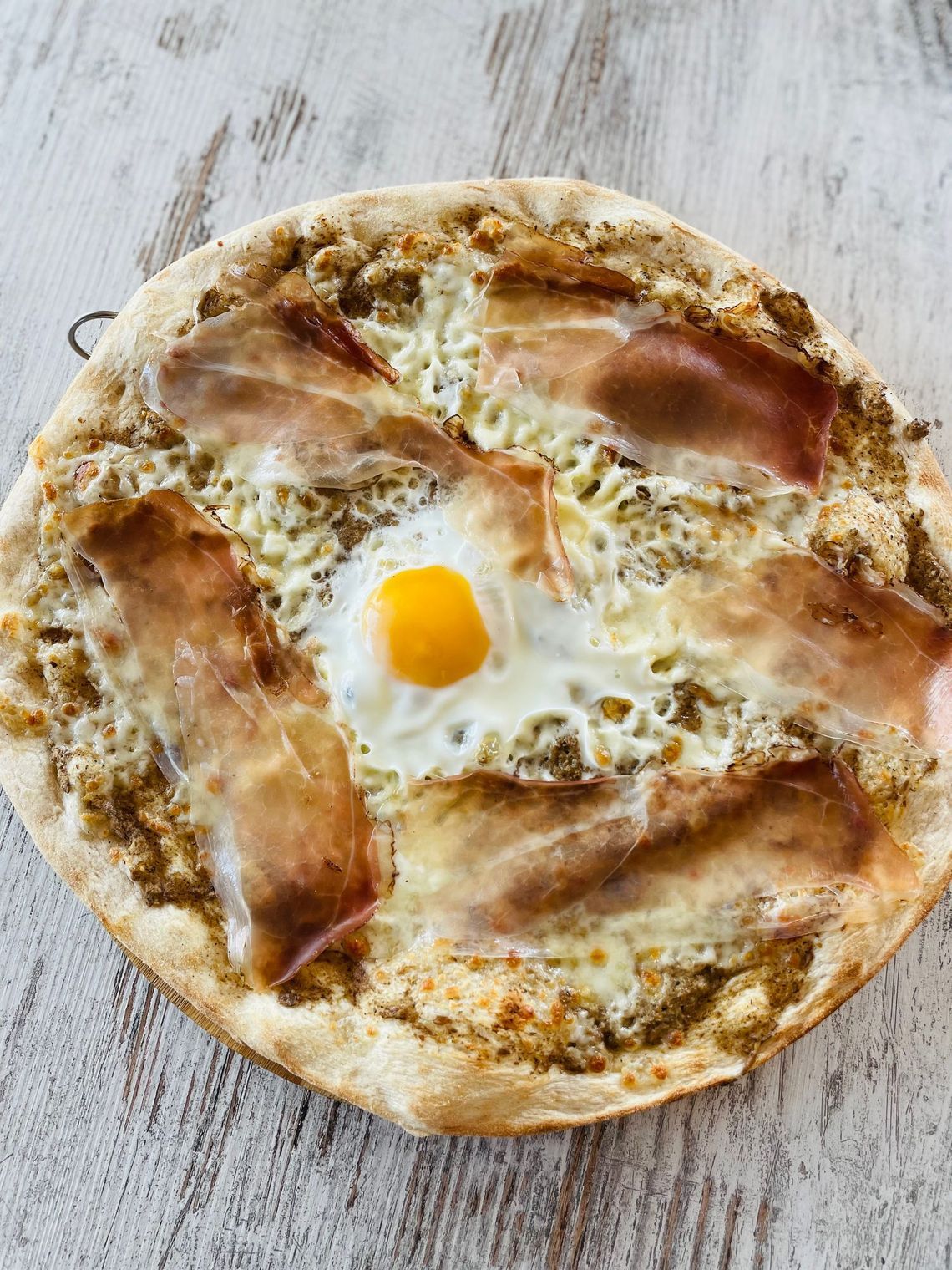 una pizza con prosciutto e uova su un tavolo di legno