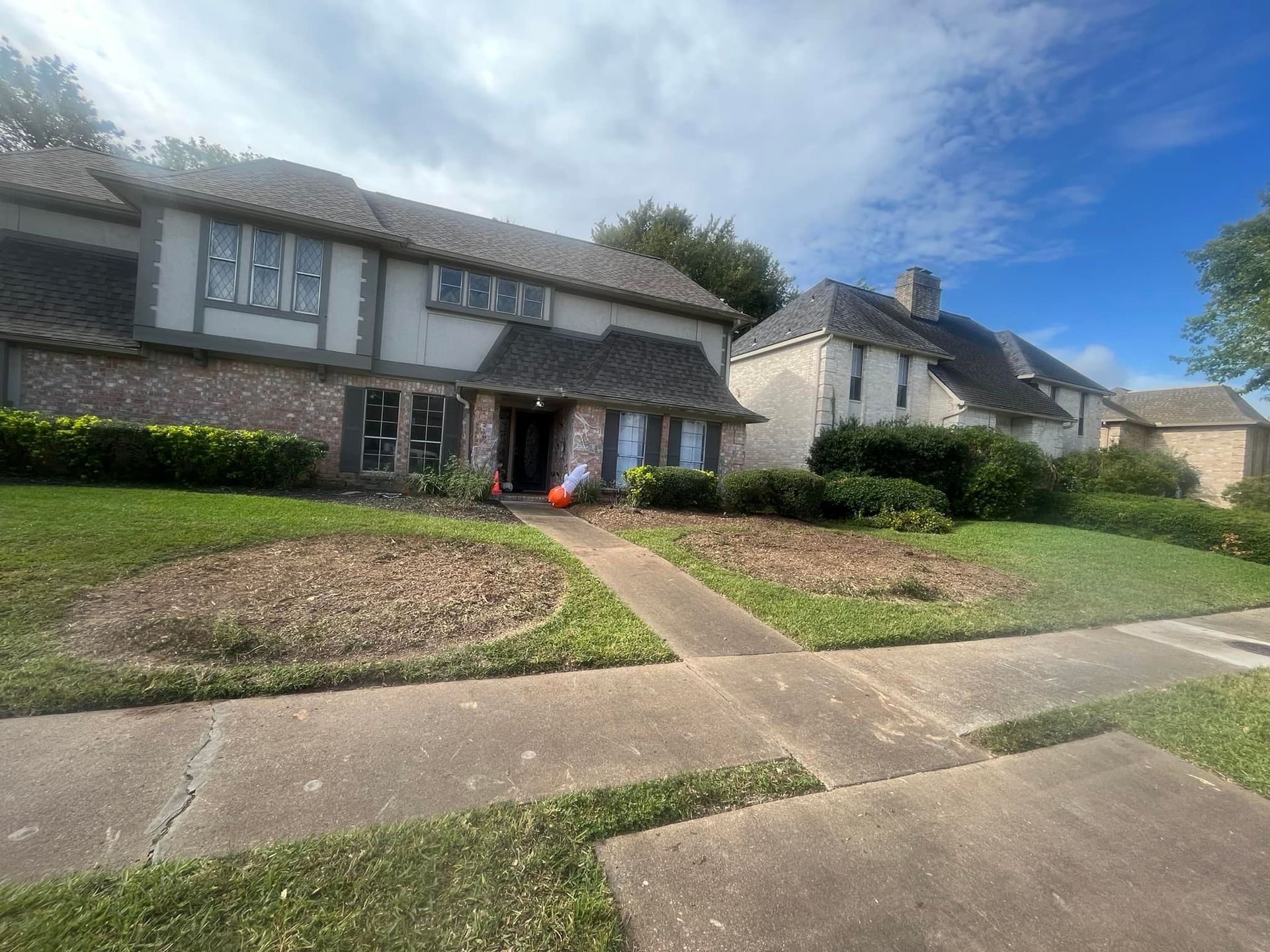 Two-story house with brick facade, concrete path, green lawn, and blue sky.