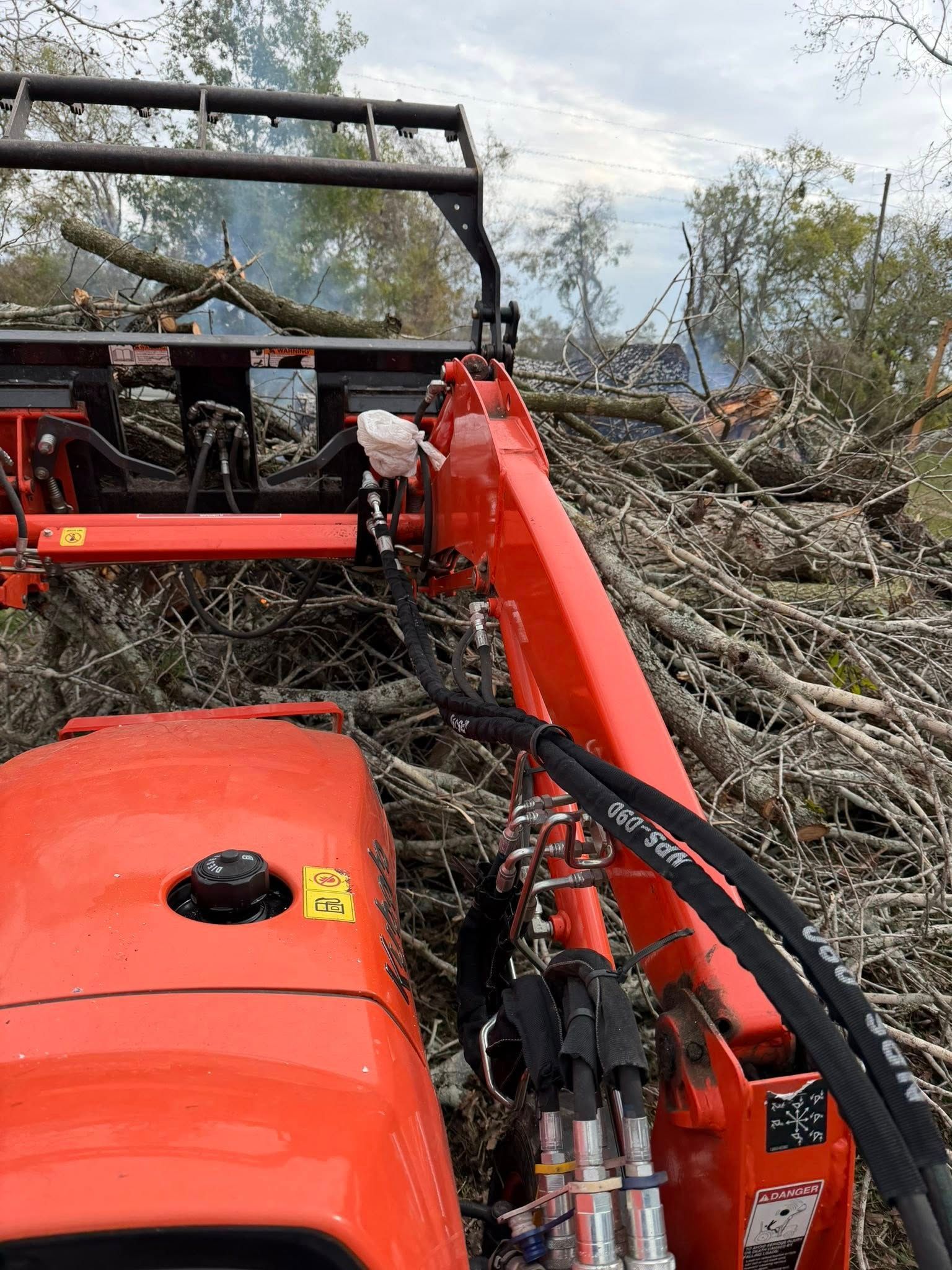 Red tractor with an extended arm clearing tree branches.