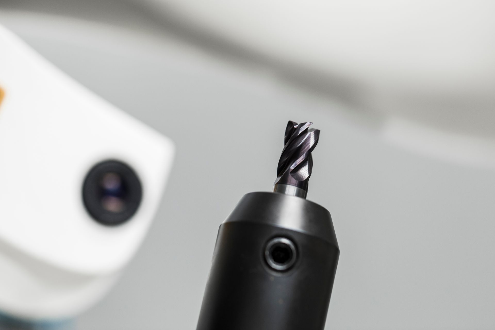 Nahaufnahme eines schwarzen Schaftfräsers, der in einem schwarzen Spannfutter eingespannt ist, vor einem verschwommenen weißen Hintergrund.