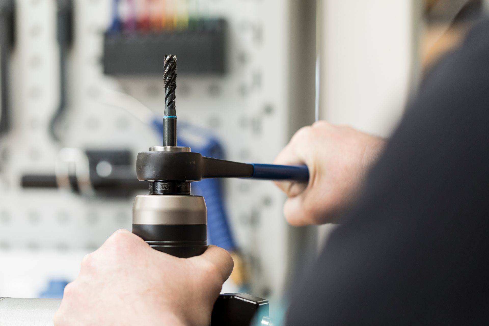 Hände, die in einer Werkstatt mit einem Schraubenschlüssel einen Bohrer in einer Bohrmaschine festziehen.