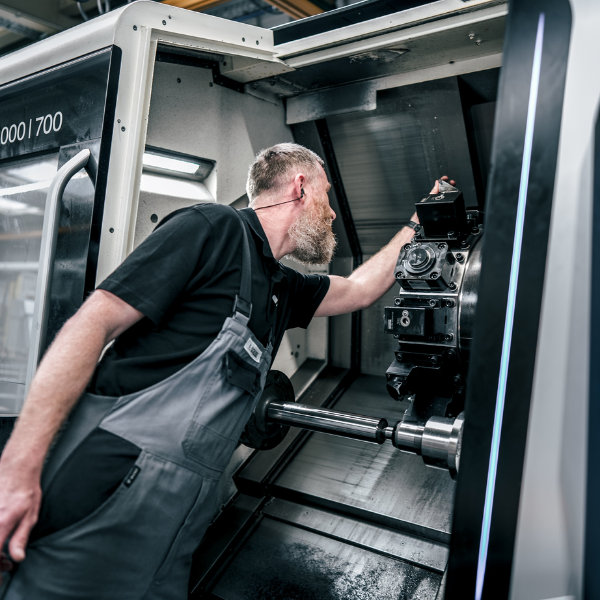 Eine Person mit Handschuhen untersucht eine Metallstange an einer CNC-Maschine.