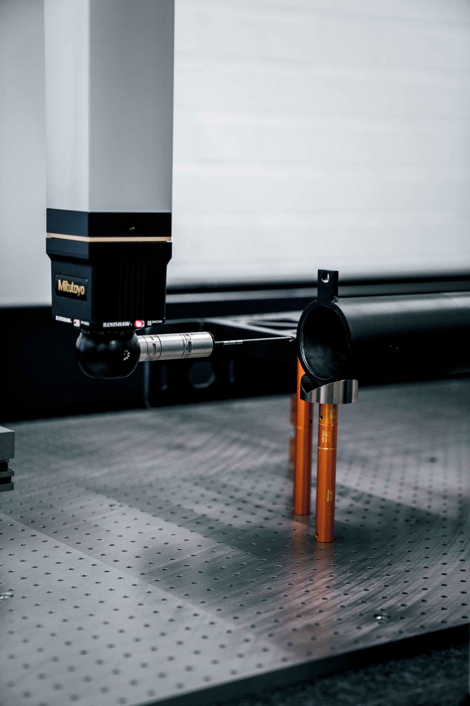 Koordinatenmessgerät prüft orangefarbene Zylinder auf einer Metalloberfläche.