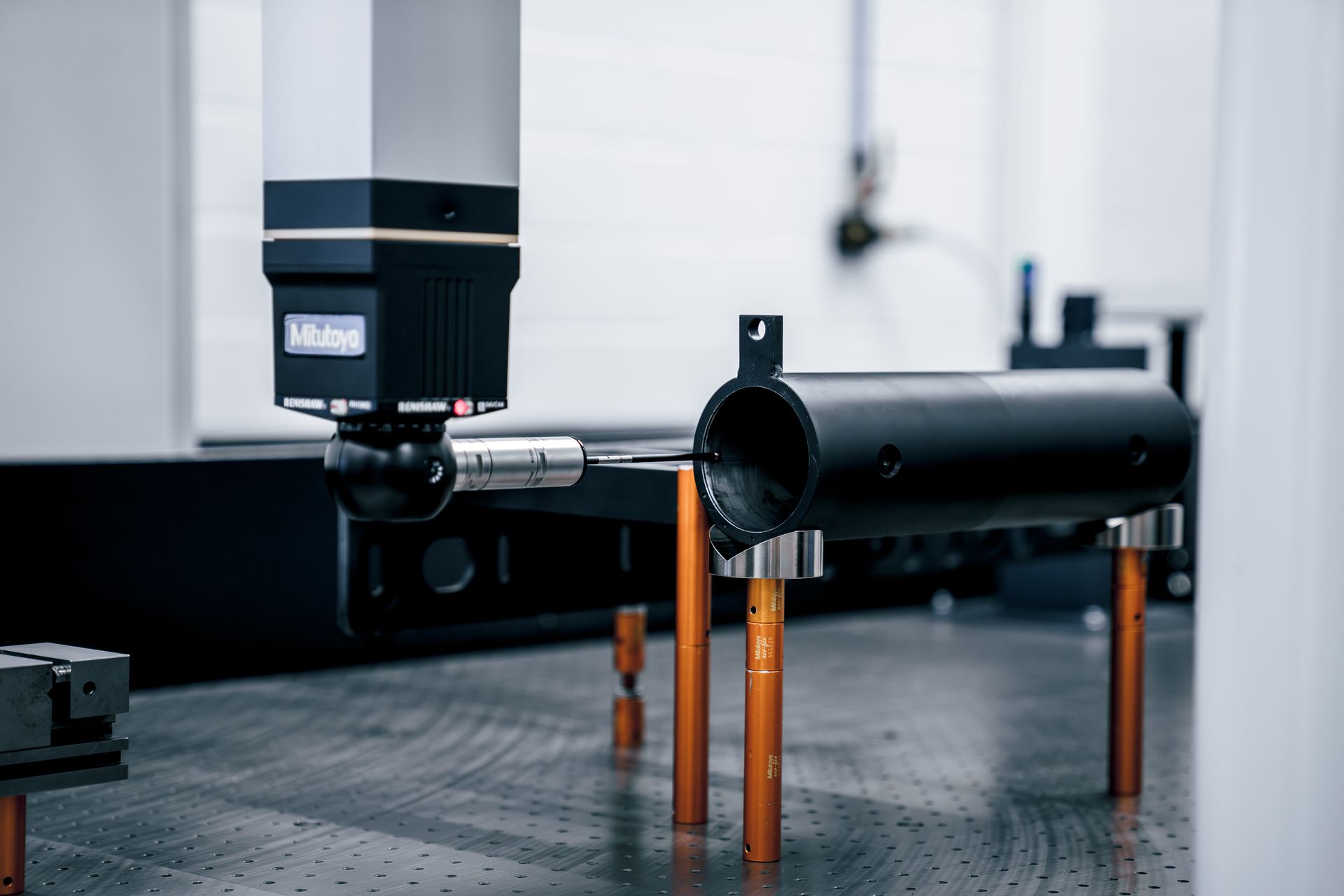 Ein schwarzes zylindrisches Teil an einer Messmaschine, das mit einem Messtaster vermessen wird.