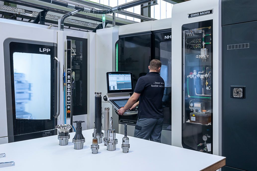 Eine Person bedient eine CNC-Maschine in einer Fabrik; Werkzeuge auf einem Tisch.