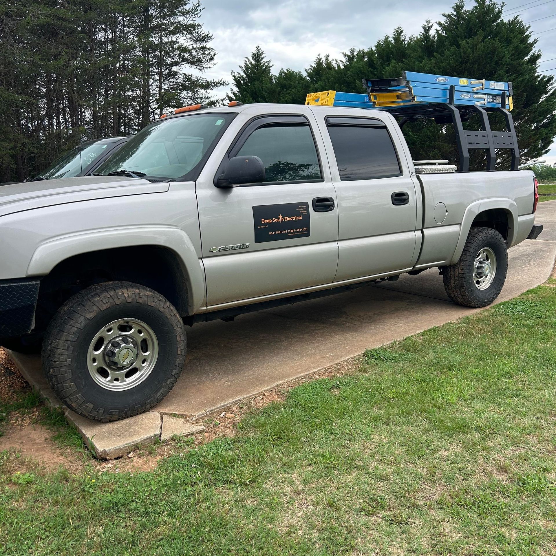 A silver truck with a ladder on the back is parked on the side of the road.