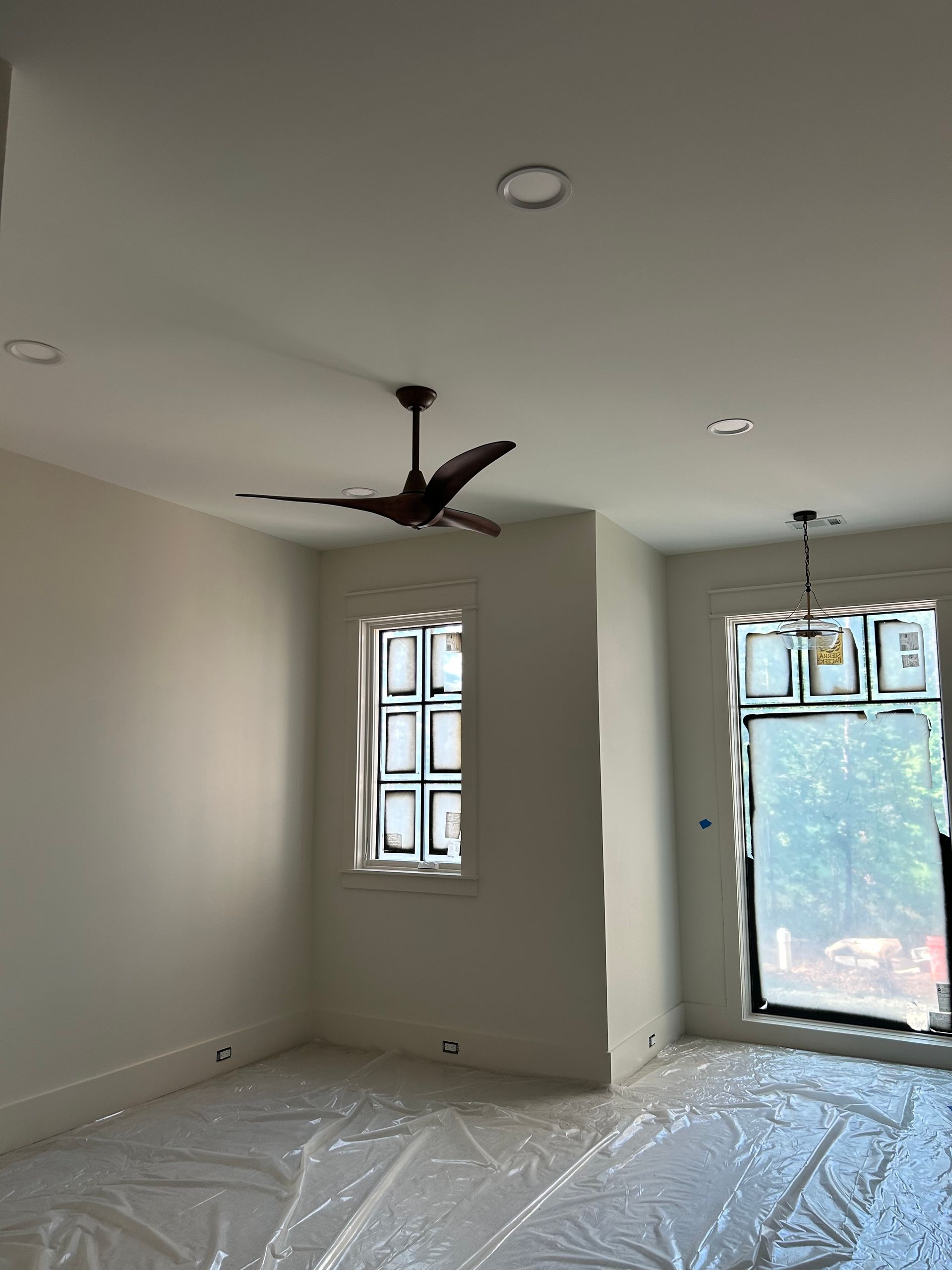 An empty room with a ceiling fan and two windows.
