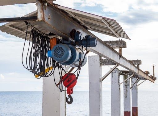 A crane is hanging from the roof of a building overlooking the ocean.