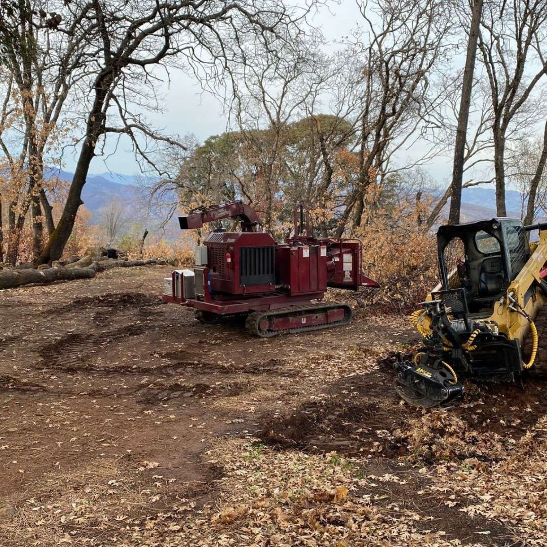 A red tractor is parked in a dirt field next to a yellow tractor.