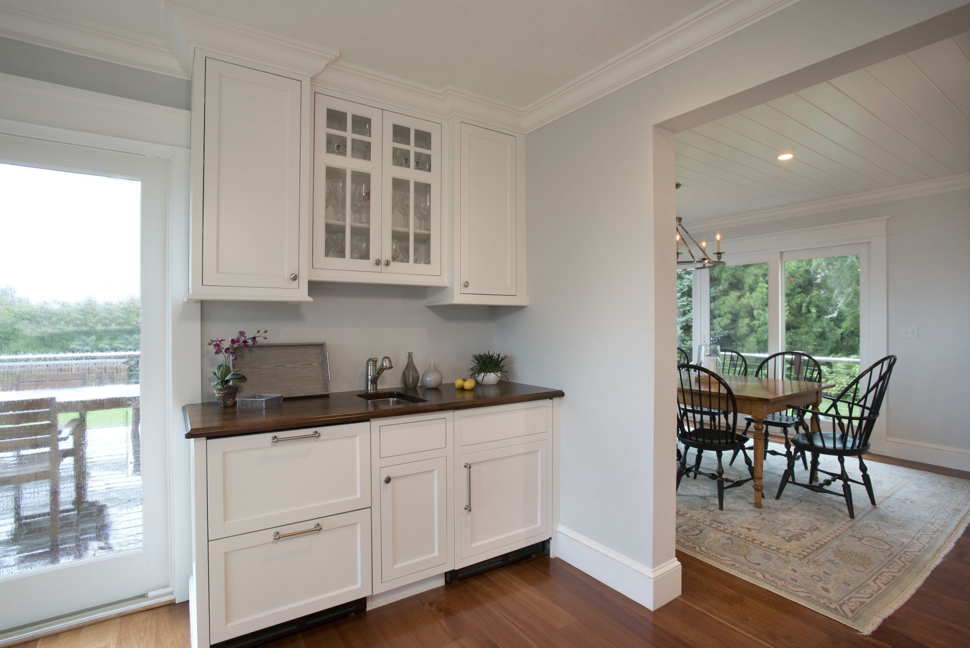 A kitchen with white cabinets and wooden floors leading to a dining room.