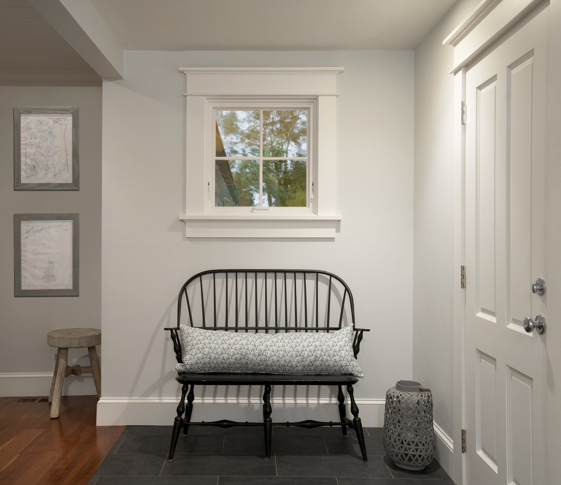 A black bench with a pillow on it is in a hallway next to a window.
