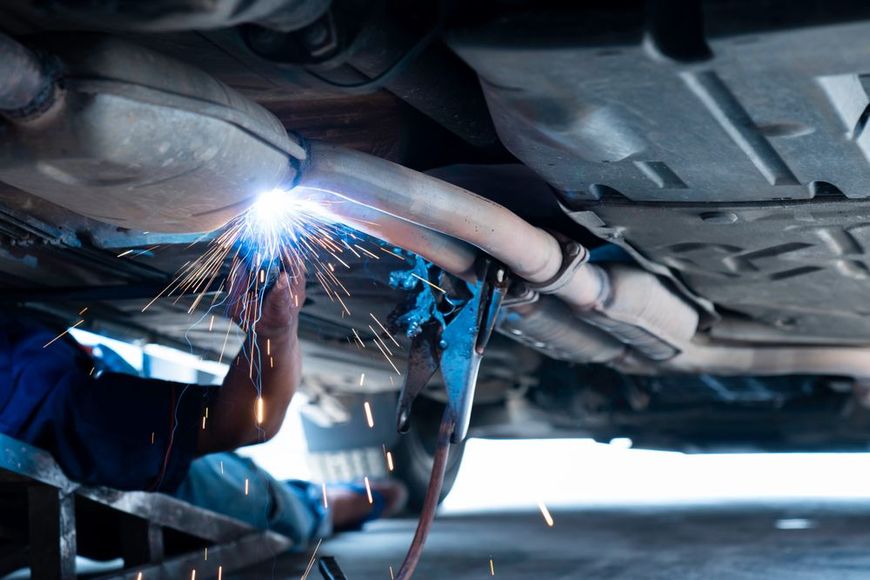 A man is welding the exhaust pipe of a car.