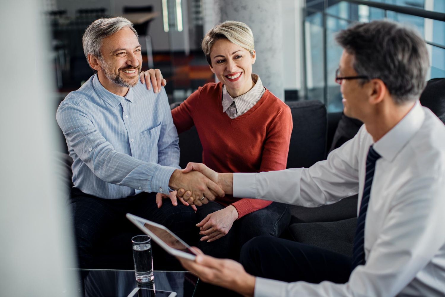Mature couple shaking hands with a professional in an office setting, smiling.