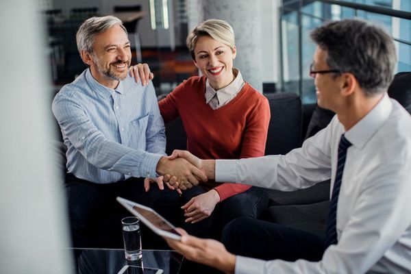 Mature couple shaking hands with a professional in an office setting, smiling.