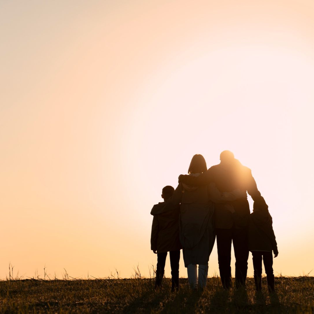 Family silhouetted against a sunset. Parents embrace two children on a hill.