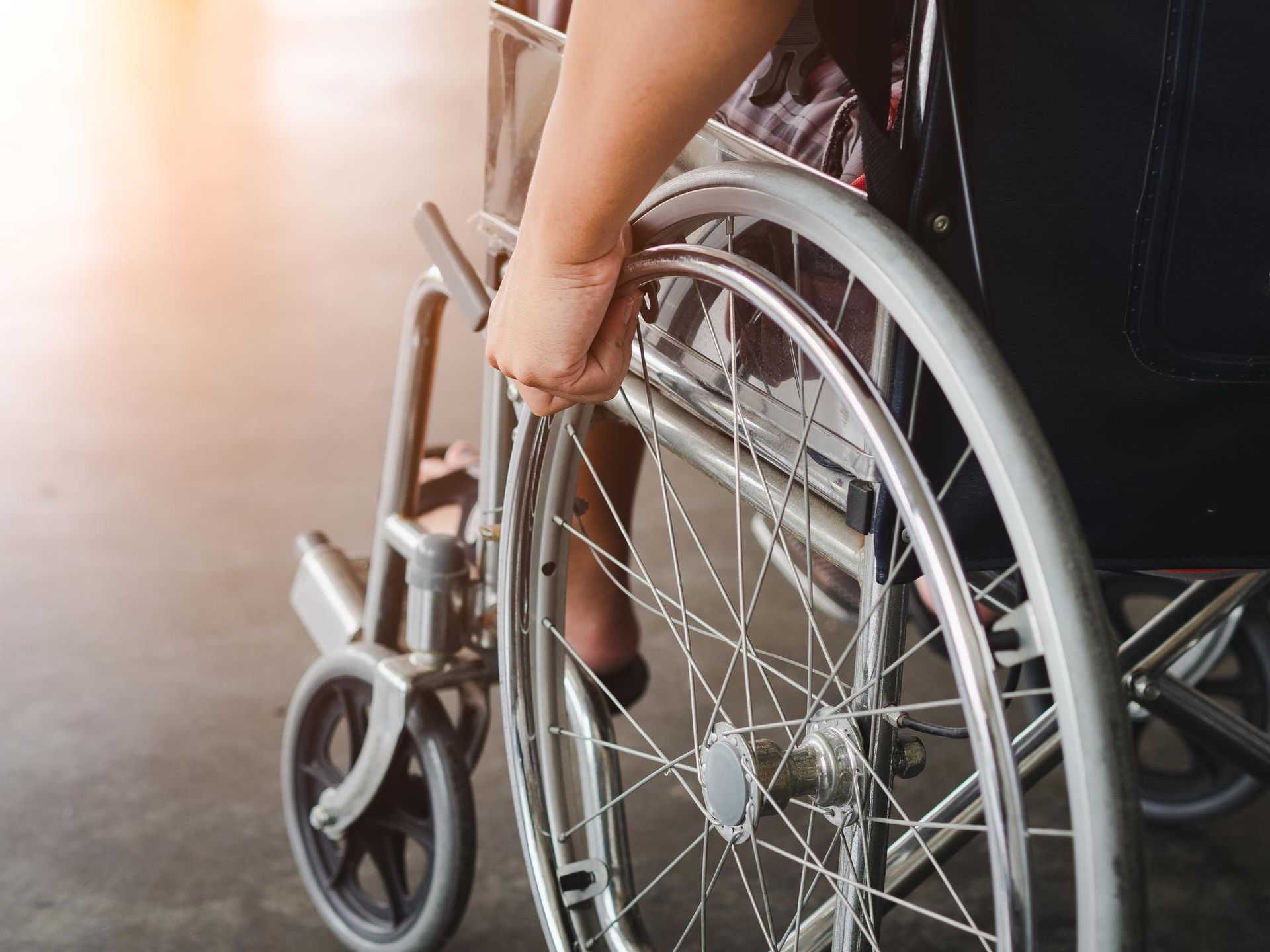 Person’s hand on the wheel of a wheelchair, indoors.