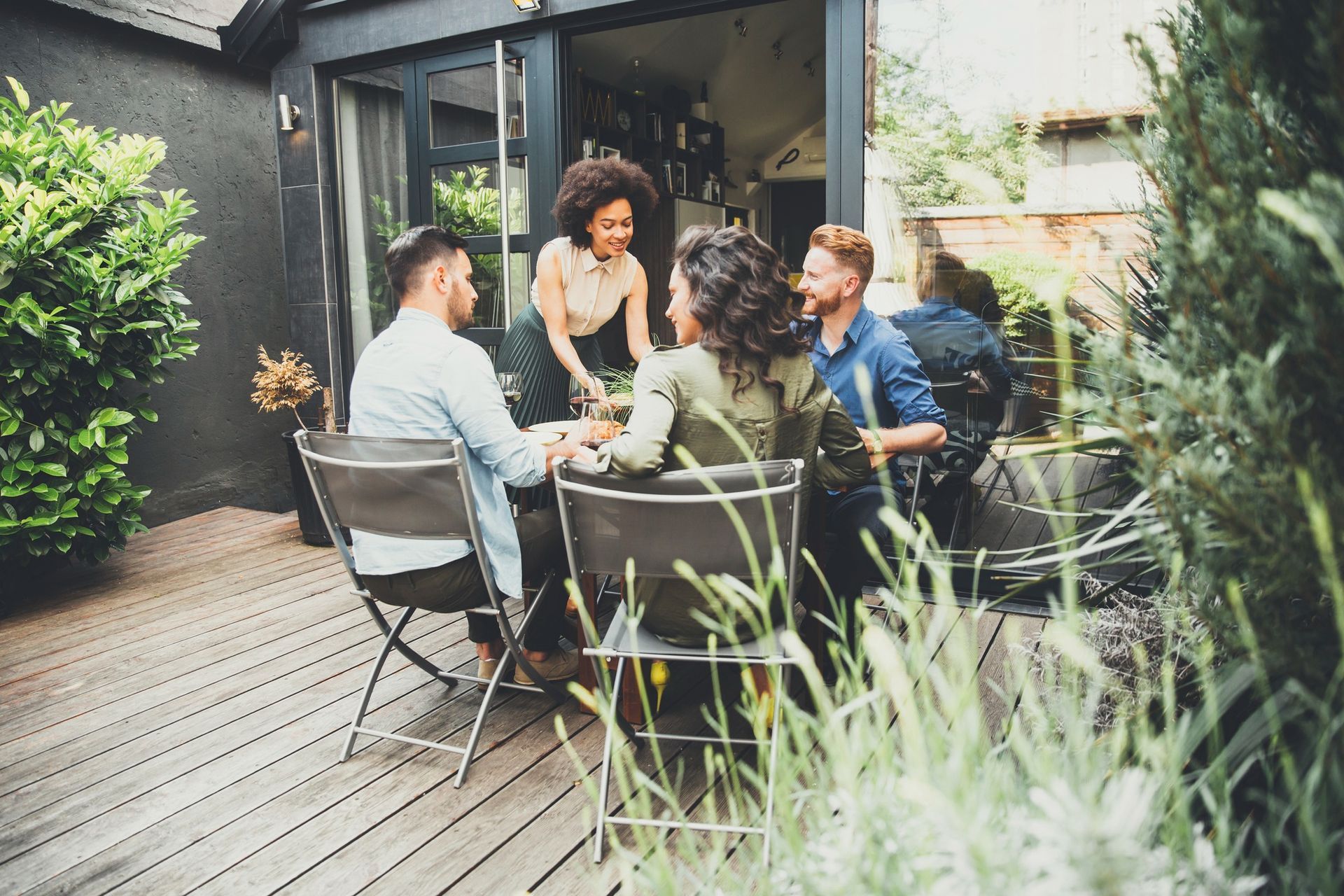 Friends gathered at an outdoor table, being served a dish, on a wooden patio.
