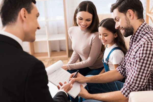 A family signs paperwork with a professional in an office setting; all appear happy.