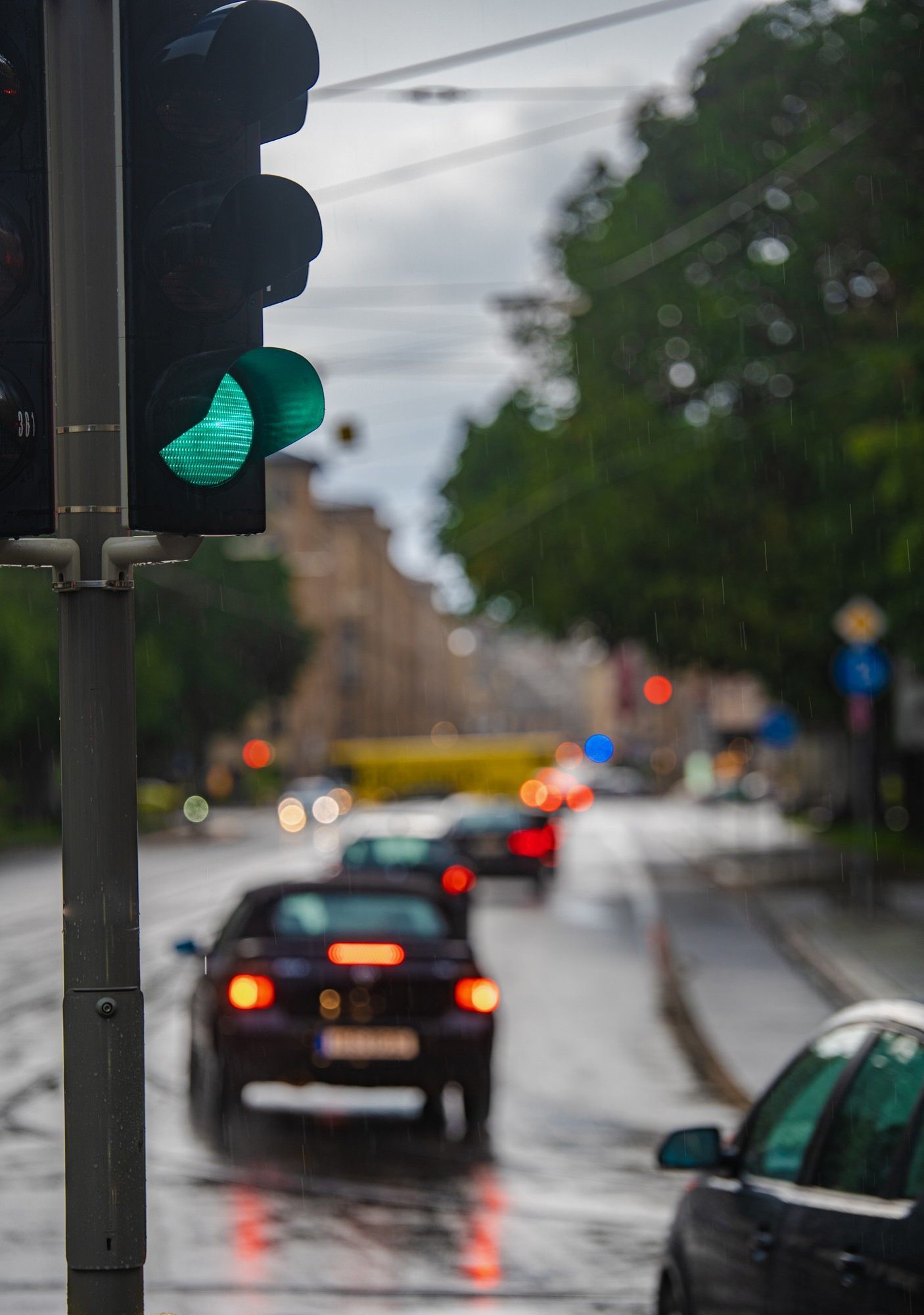 Green traffic light; cars on wet street, rain; blurred background of buildings.