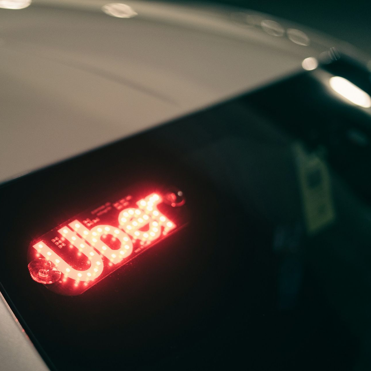 Light-up Uber sign in red on a car's rear window.