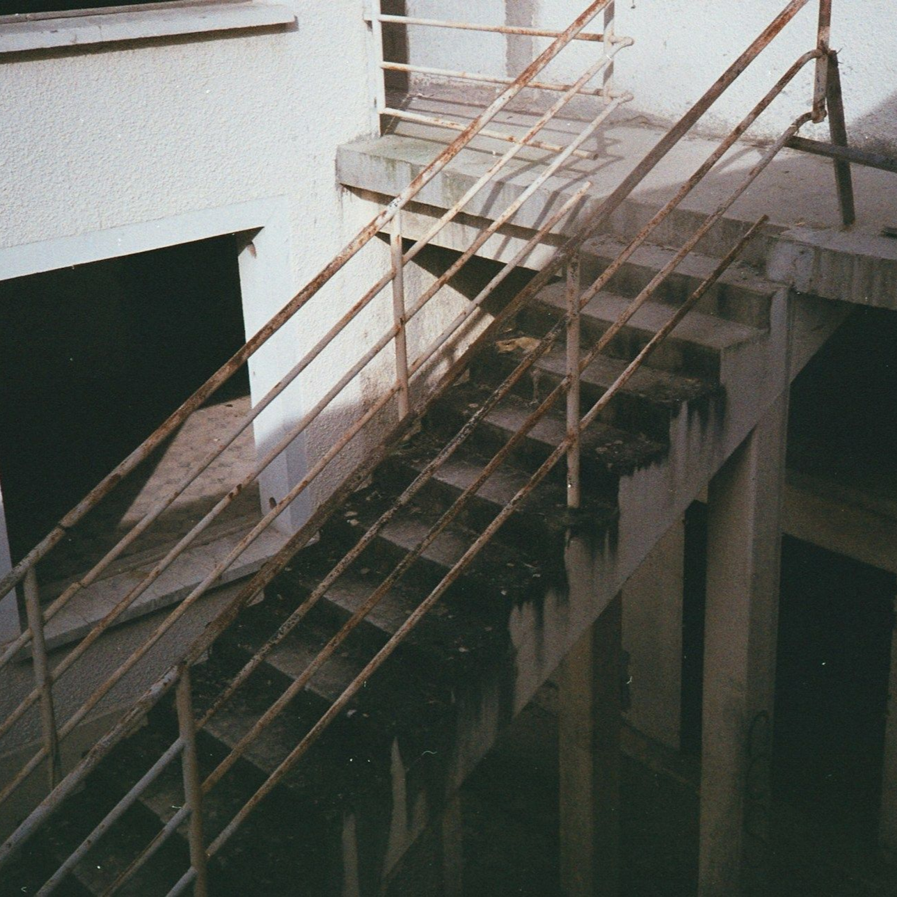 Rusty outdoor staircase leading up, attached to a building with off-white walls.