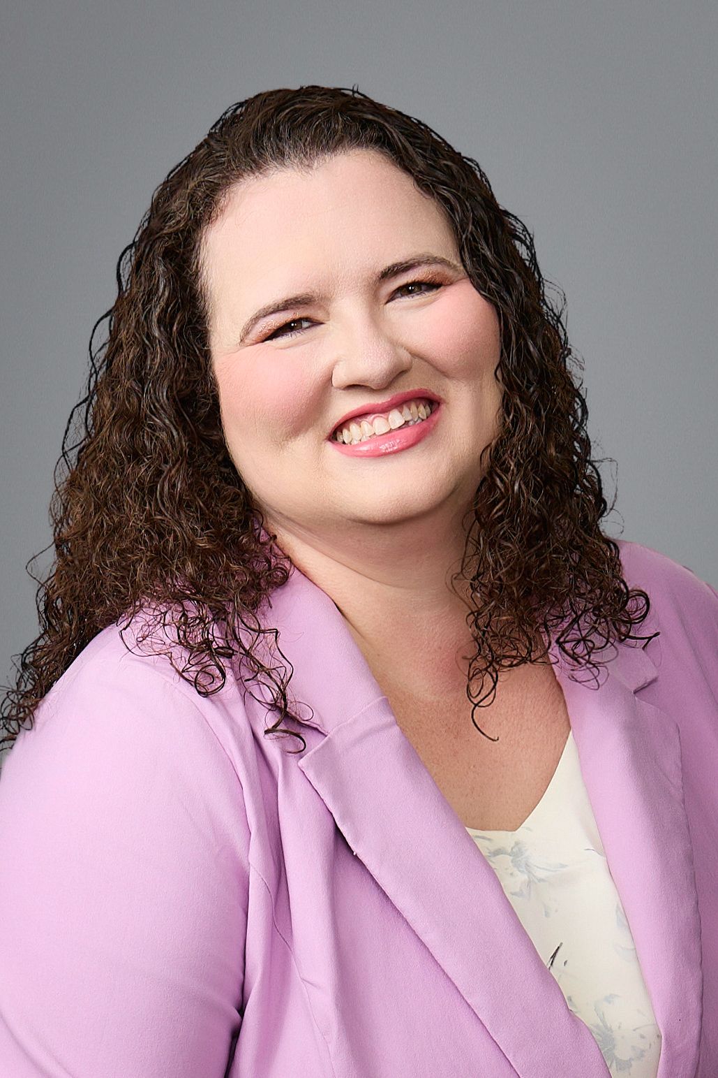 A woman wearing glasses and a red jacket is smiling.