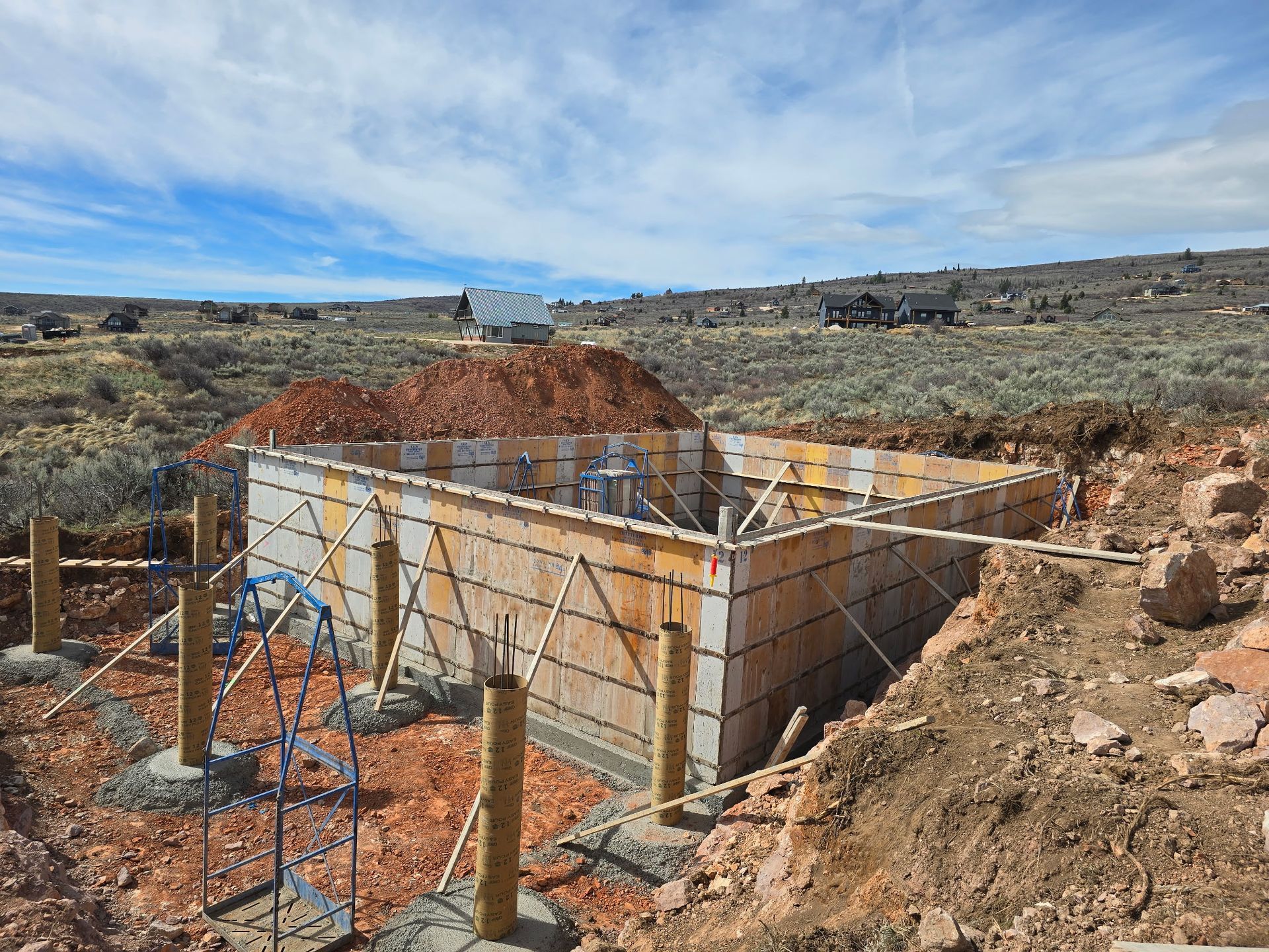 Construction site with concrete foundation walls and rebar in a dry, rocky landscape under a blue sky