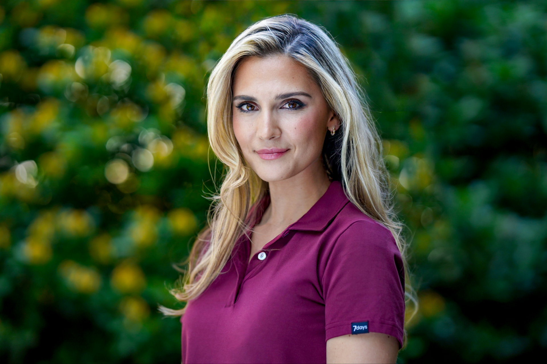 En kvinne i en lilla poloskjorte står foran en busk.