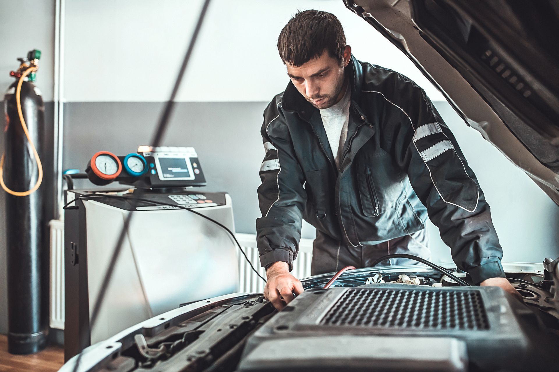A male young auto mechanic doing service of car's air conditioning system in repair shop.