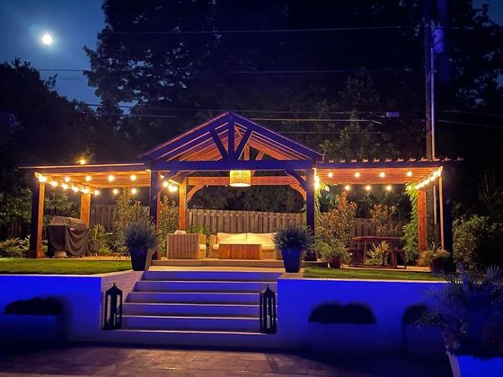 A gazebo is lit up at night in a backyard.