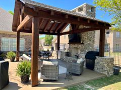 A wooden pavilion with a fireplace and a grill in the backyard of a house.