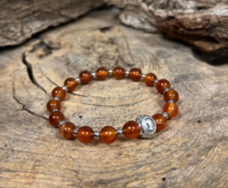 Armband met oranje edelstenen op een kaartje met illustratie van het sterrenbeeld Maagd. De tekst luidt: Carneool, Maagd.