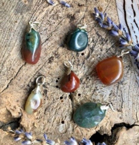 Zes gepolijste edelsteenhangers op een verweerd houten oppervlak, met lavendel en een veer.