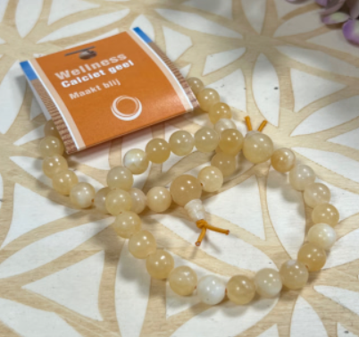 Kralenarmband met geelbeige stenen en een geknoopt kwastje op een witte achtergrond.