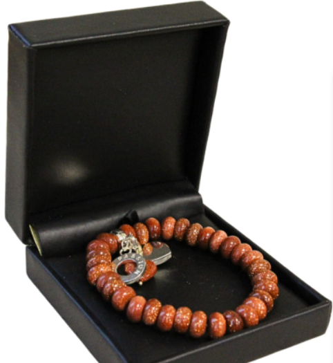 Armband van goudkleurige kralen in een zwart geschenkdoosje.