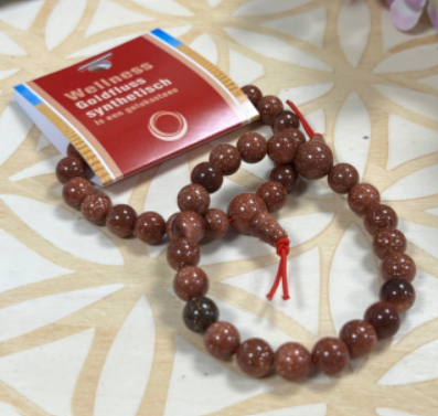 Armband van bruine en gouden edelstenen met een rood koord en een kraal aan het uiteinde.