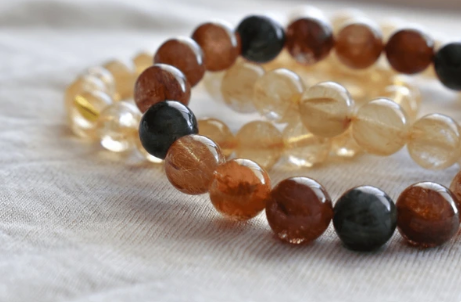 Twee armbanden met edelstenen kralen, met amberkleurige, zwarte en gele kralen, liggen op een witte doek.