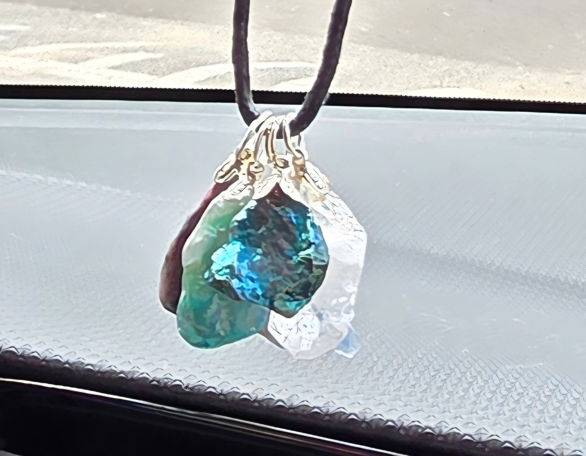 Hanger met blauwe, groene en heldere kristallen stenen, hangend aan een zwart koord, die het zonlicht weerkaatsen.