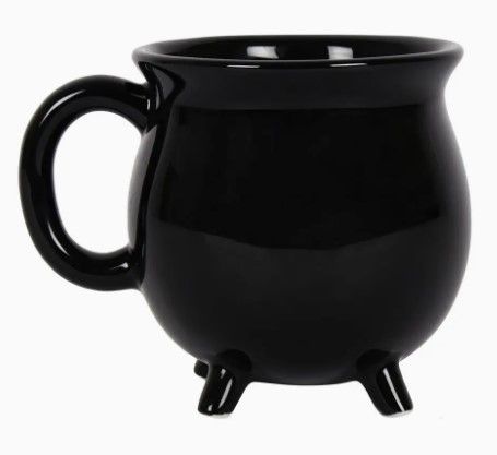 Zwarte, ketelvormige mok en drie kleine pootjes, geplaatst tegen een griezelige Halloween-bosscène met gloeiende pompoenen.