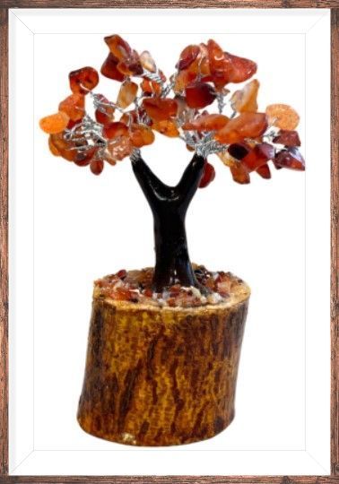 Kristallen boomsculptuur met oranje edelstenen, bruine stam op een houten voetstuk, tegen een vage florale achtergrond.