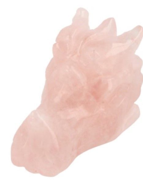 Twee drakenkoppen van rozenkwarts op een houten oppervlak, met roze bloemen en een zoutlamp op de achtergrond.