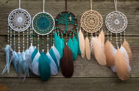 Dromenvangers met turquoise, bruine en beige veren hangen tegen een verweerde houten achtergrond.