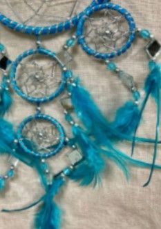 Blauwe dromenvanger met veren, kralenaccenten en een centraal web, hangend op een neutraal oppervlak.