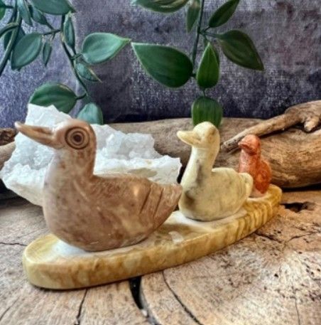 Drie stenen eendenbeeldjes op een gebogen voetstuk, in verschillende tinten bruin en lichtbruin.