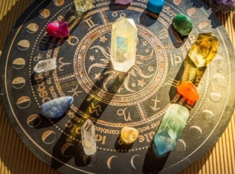 Een zwarte, ronde dierenriemkaart met daaromheen kleurrijke kristallen, verlicht door zonlicht.