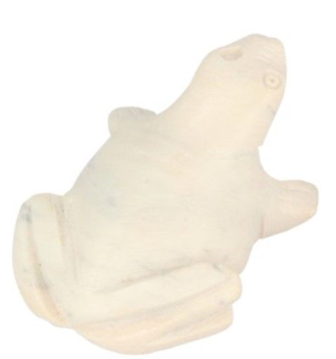 Wit stenen kikkerbeeld op een getextureerd houten oppervlak, omgeven door groene bladeren.