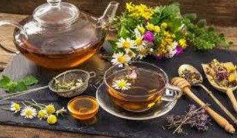 Glazen theepot en theekopje met bloemen, kruiden en honing op een houten tafel.