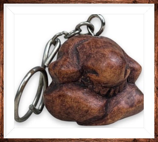 Twee bruine sleutelhangers met op een houten oppervlak, met een onscherpe achtergrond van drijfhout en bloemen.